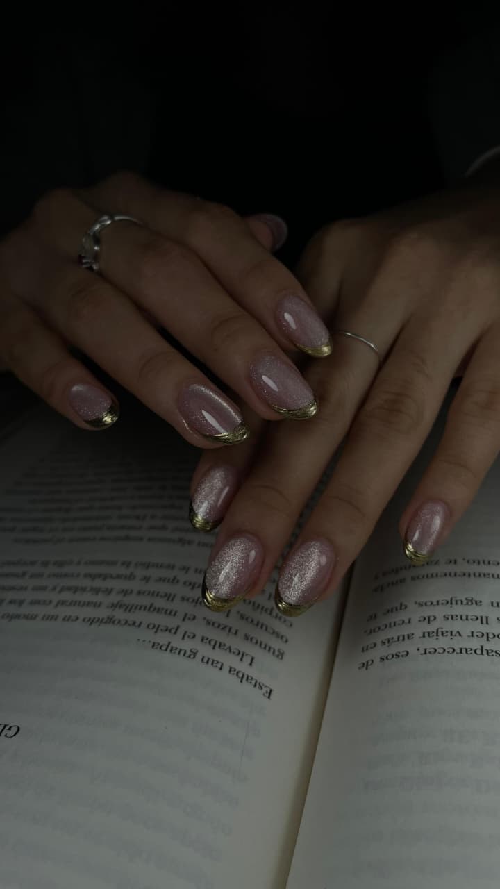 Uñas brillantes con punta dorada en fondo oscuro
